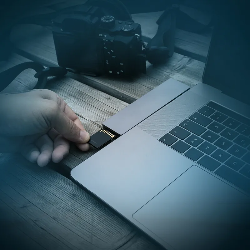 A memory card being inserted into a laptop with a camera beside it